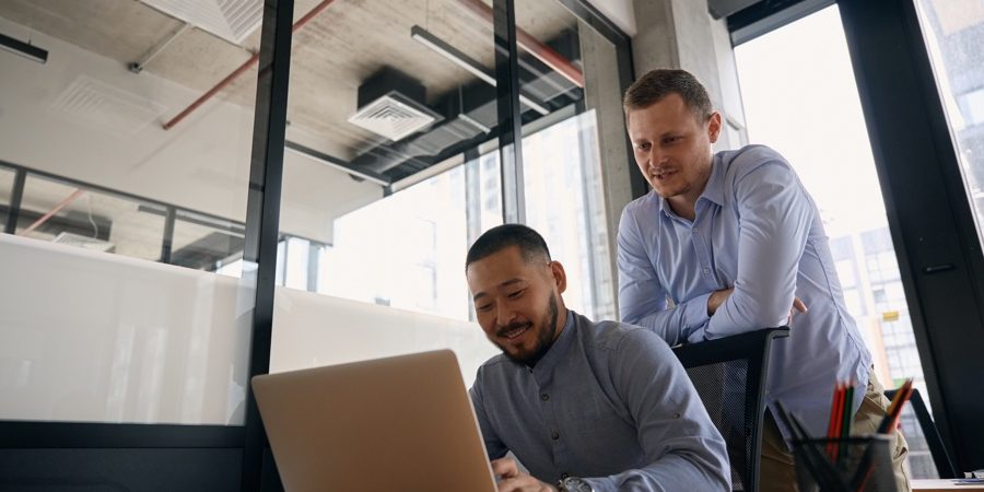 Smiling company worker entering data into portable computer supervised by office colleague